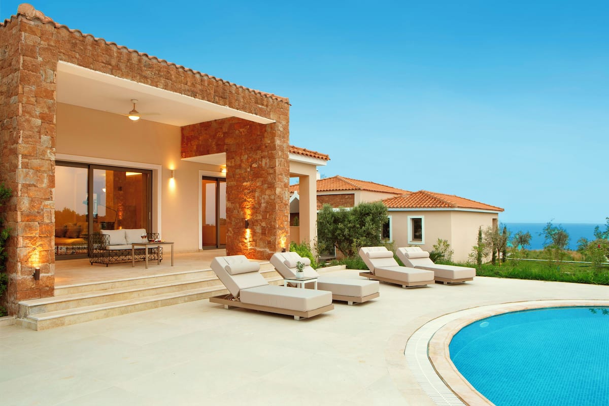 Una casa moderna con piscina, mobiliario exterior y vista al mar.