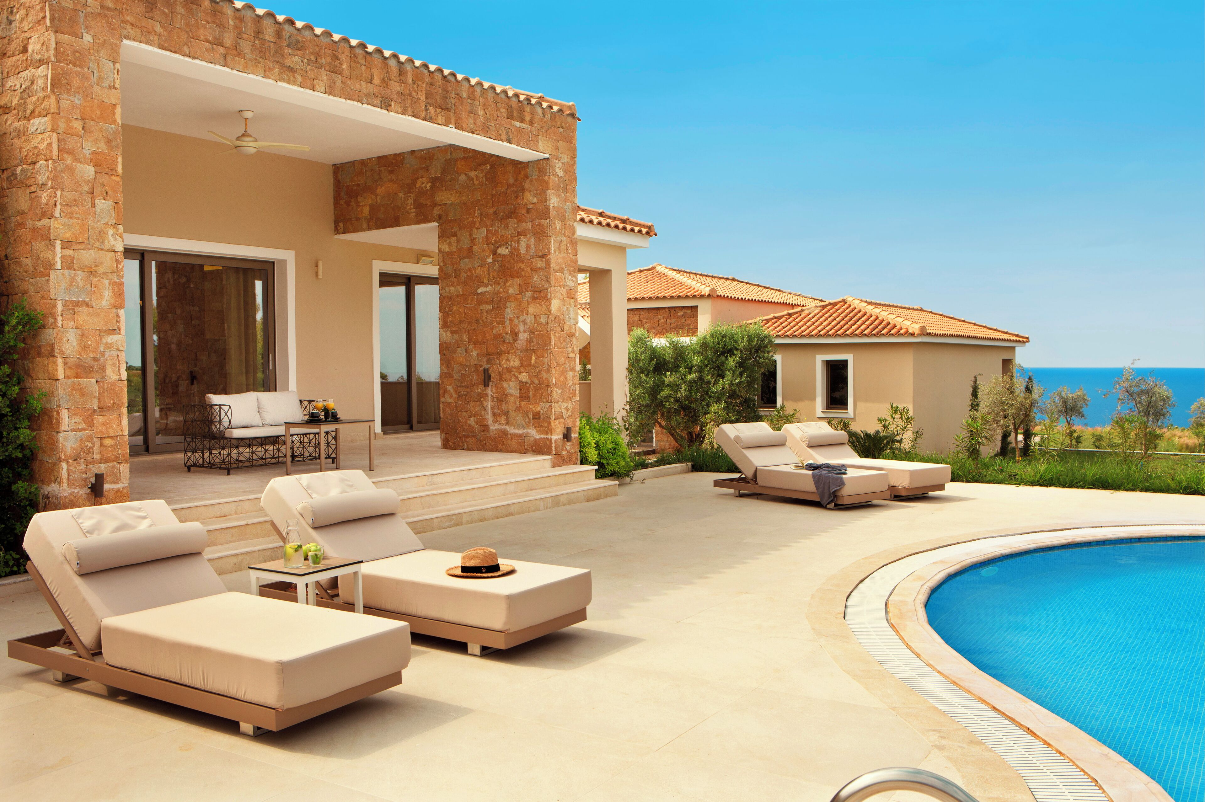 A poolside area with lounge chairs, a table, and a view of the sea.