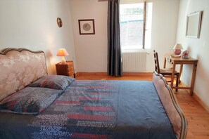 Une chambre à coucher avec un lit, une table de chevet, une chaise, une table et une fenêtre avec des rideaux.
