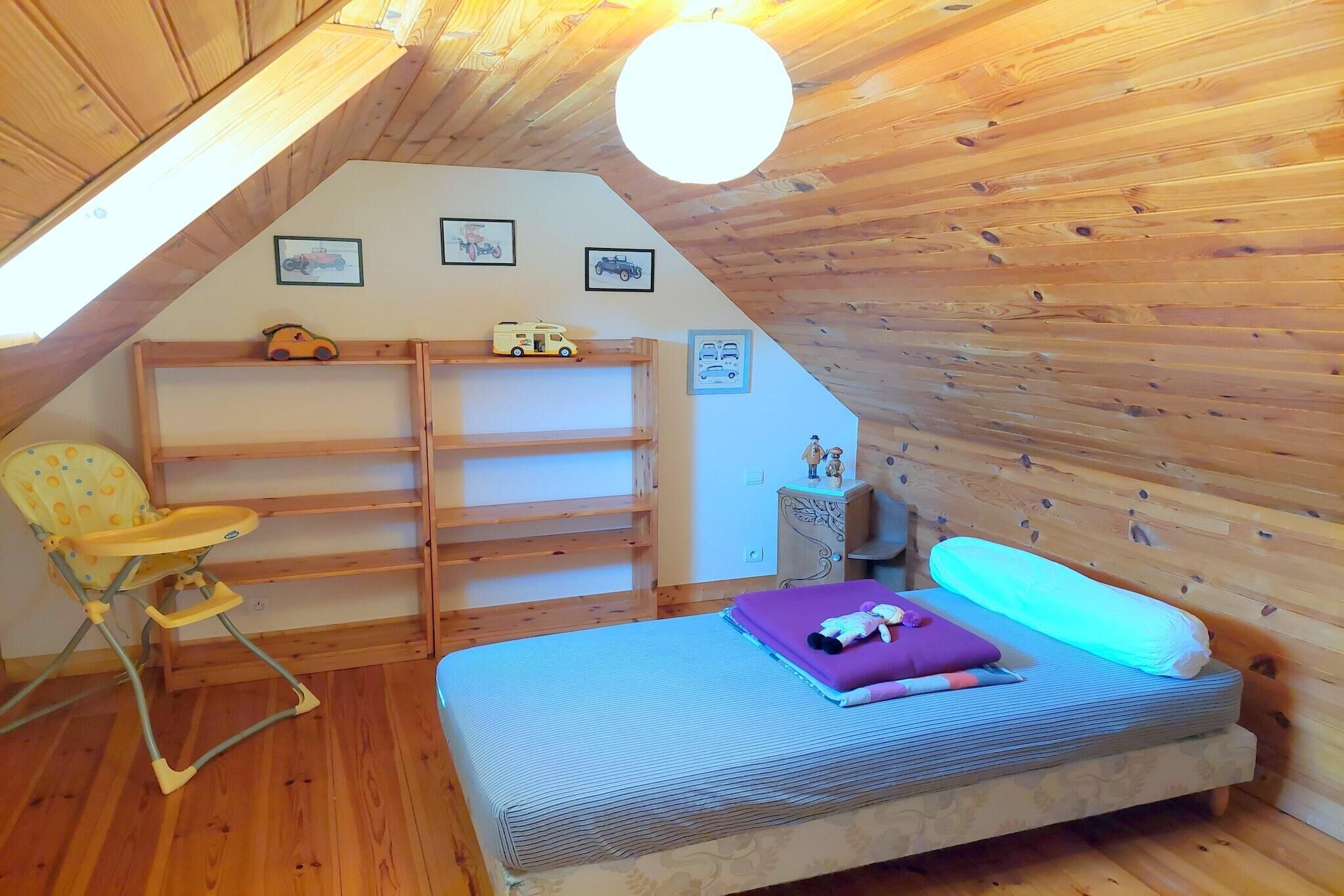Une chambre mansardée chaleureuse avec un plafond en pente, des murs en bois, un lit superposé, une chaise haute et un petit bureau.