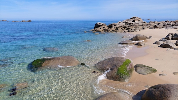 Una playa con agua cristalina, grandes rocas y islas a lo lejos.