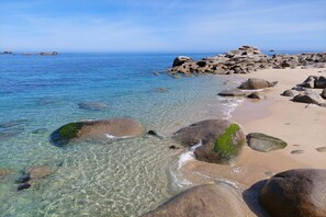 Une plage à l’eau claire, bordée de gros rochers et offrant une vue sur des îles lointaines.