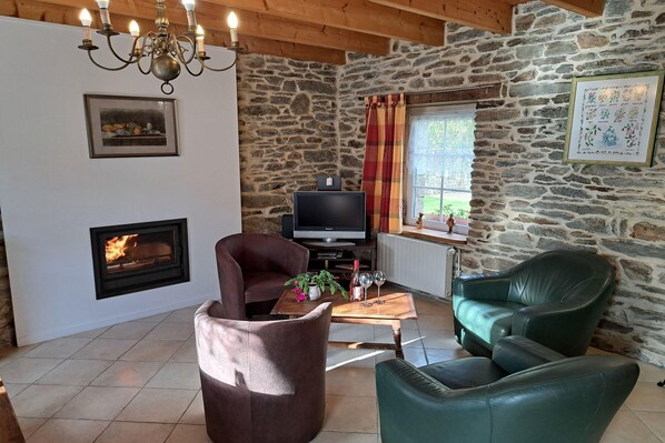 Un salon chaleureux avec une cheminée, des murs en pierre et des fauteuils en cuir confortables.