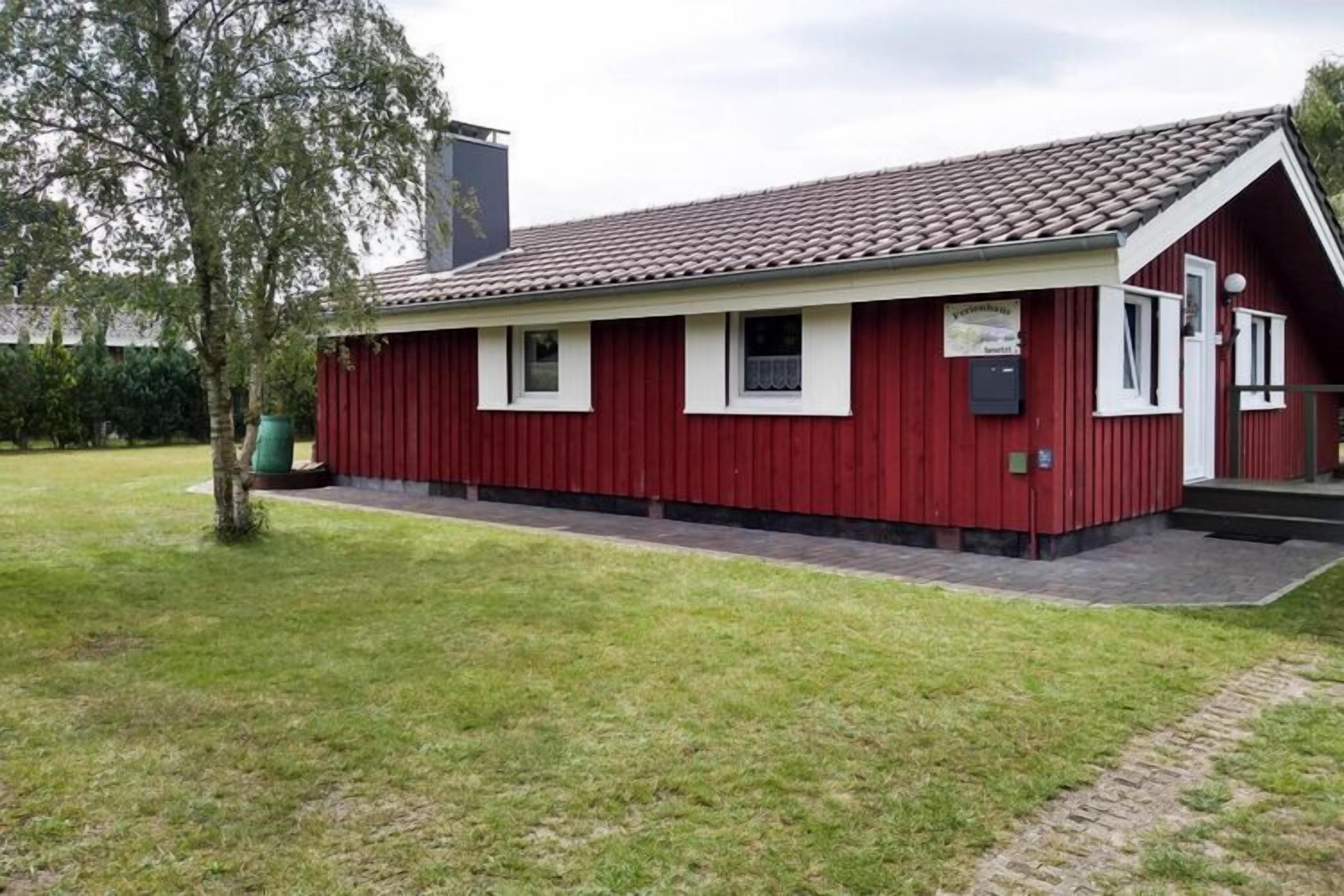 A red building with a tiled roof, a small porch, and a green trash bin.