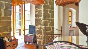 A cozy room with stone walls, a wooden floor, a television, a wicker basket, and a striped chair. - Chalet in Styria with Pool & Panoramic Views (Fehring)