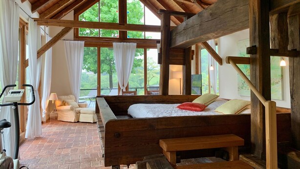 A rustic bedroom with a wooden bed, a bench, a treadmill, and large windows offering a view of greenery. - Chalet in Styria with Pool & Panoramic Views (Fehring)