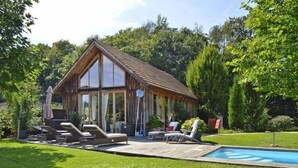 A wooden cabin with a swimming pool, deck chairs, and a covered patio area. - Chalet in Styria with Pool & Panoramic Views (Fehring)