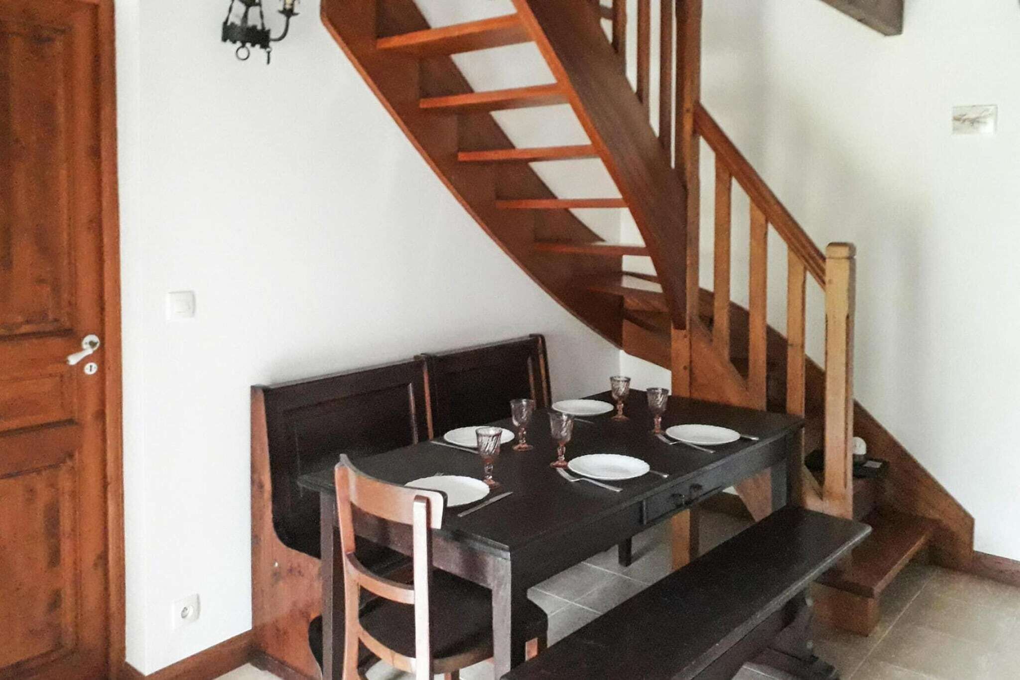 Un coin repas avec un escalier en bois, une table dressée pour quatre personnes et un banc.