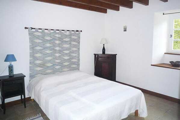 A bedroom with a bed, a nightstand, a lamp, a dresser, and a window with a view.