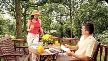 A wooden deck with a table, chairs, and a person reading a book.