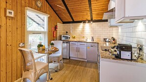Une cuisine compacte aux murs en bois, un coin repas avec des chaises en osier et un dosseret de carrelage blanc.