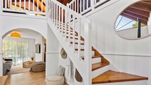 A spacious interior with a wooden staircase, a cozy seating area, and a large window providing natural light.
