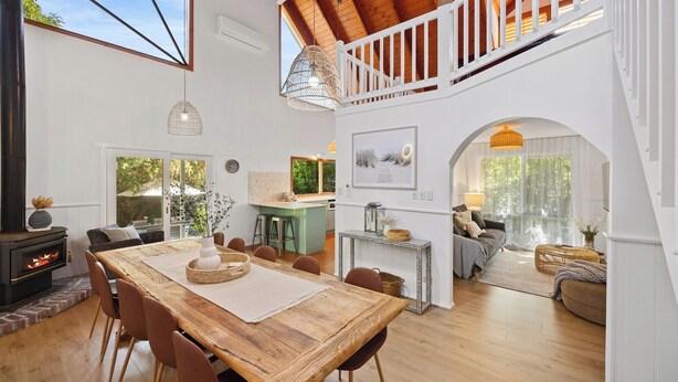 A spacious living area with a high ceiling, wooden beams, a dining table, and a cozy seating area with a sofa and chairs.