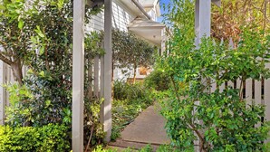 A covered garden pathway leading to a building with a white facade and a wooden pergola structure.