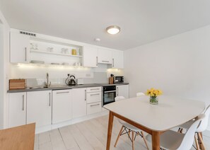 A modern kitchen with white cabinetry, a built-in oven, and a dining area with a white table and chairs.