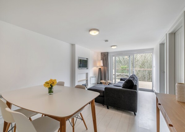 Un salon moderne comprenant un canapé, une table à manger avec des chaises, un téléviseur fixé au mur et un balcon avec vue.