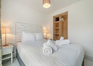 Une chambre d’hôtel avec un lit, des lampes de chevet, une armoire en bois et une serviette sur le lit.