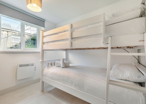 A bunk bed room with a window, radiator, and a hanging light fixture.