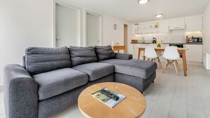 Ett modernt vardagsrum med en grå hörnsoffa, ett runt soffbord i trä och en matplats med ett vitt bord och stolar.