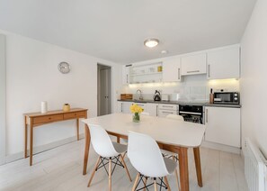Una cocina moderna con armarios blancos, una mesa de comedor con dos sillas, un reloj y un microondas.