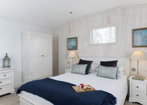 Ein Schlafzimmer mit einem Bett, Nachttischen, einem Kleiderschrank und zwei Fenstern.