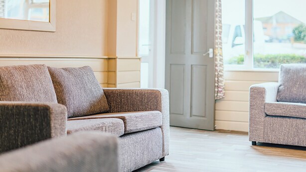 Un salon avec un canapé et un fauteuil, une porte et une fenêtre avec des rideaux.