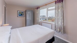 Une chambre à coucher avec un lit, une armoire, une fenêtre avec des rideaux et un radiateur.