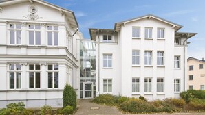 Ein modernes Gebäude mit zentralem Glas Eingang, weißer Fassade und zahlreichen Fenstern.