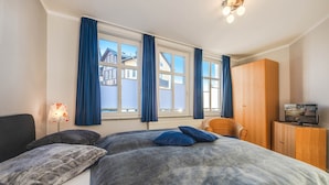 Ein Schlafzimmer mit einem großen Bett, zwei Kissen, einem Holzschrank, einem Fernseher und einem Fenster mit Vorhängen.