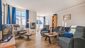Ein modernes Wohnzimmer mit einer Couch, Sesseln, einem Couchtisch und einem Fernseher.