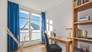 Ein Zimmer mit einem Holztisch, einem Stuhl, einem Bücherregal und einem Fenster mit blauen Vorhängen.