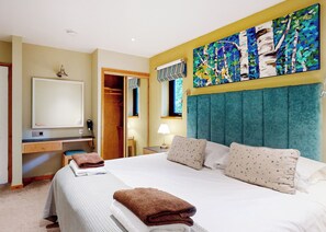 A hotel room with a bed, a desk, a mirror, a wardrobe, and a painting on the wall.