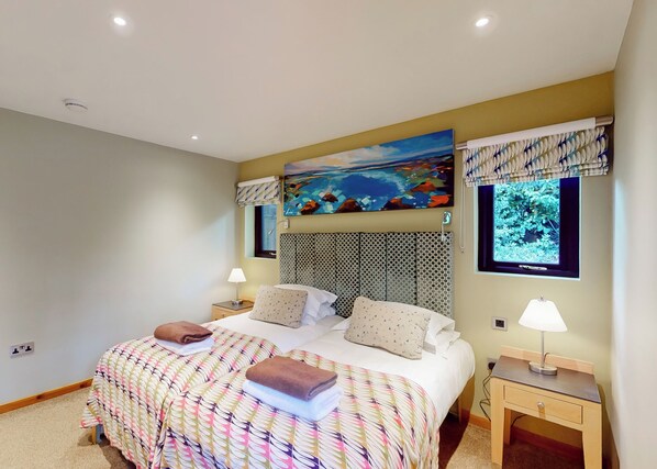 Une chambre à coucher avec un lit, deux tables de chevet, une fenêtre donnant sur un paysage agréable, un tableau au mur et un luminaire au plafond.