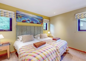 A hotel room with a bed, two bedside tables, a nightstand, a painting, and a window with a curtain.