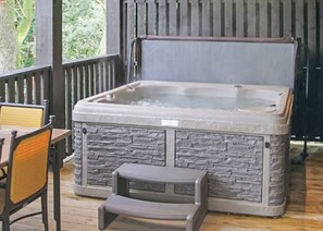 A hot tub with a stone exterior, a wooden deck, and a small step stool.