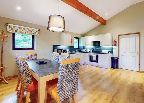 A modern kitchen with a dining area, wooden flooring, and a large window with a view.