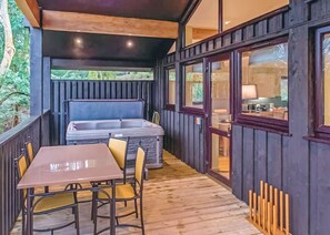 A wooden deck with a hot tub, a table, and chairs.