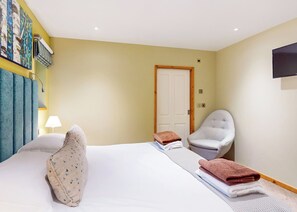 A hotel room with a bed, a chair, a lamp, and a door.