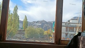 A view through a window with a mountain landscape, trees, and buildings in the background. - Munna Palace  (Leh)