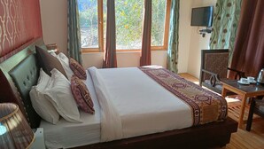 A neatly made bed with a patterned bedspread, a wooden nightstand with a lamp, a chair, and a table with cups and a kettle. - Munna Palace  (Leh)