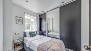 Una camera da letto con un letto, un comodino, una lampada, una finestra e uno specchio.