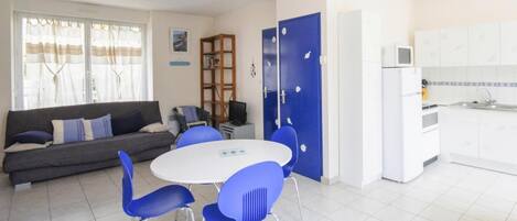 Ein modernes Wohnzimmer mit Sofa, Esstisch mit Stühlen, Küchenzeile und einer blauen Tür.