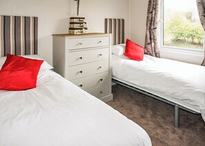 A bedroom with two beds, a dresser, and a window with curtains. - 3 bedroom accommodation in Carnforth (Carnforth)