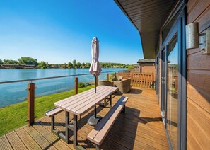 A wooden deck with a table and benches overlooking a lake. - 3 bedroom accommodation in Carnforth (Carnforth)