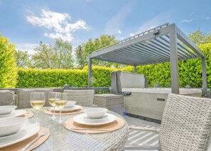An outdoor patio with a covered seating area, a table set for dining, and a grill.