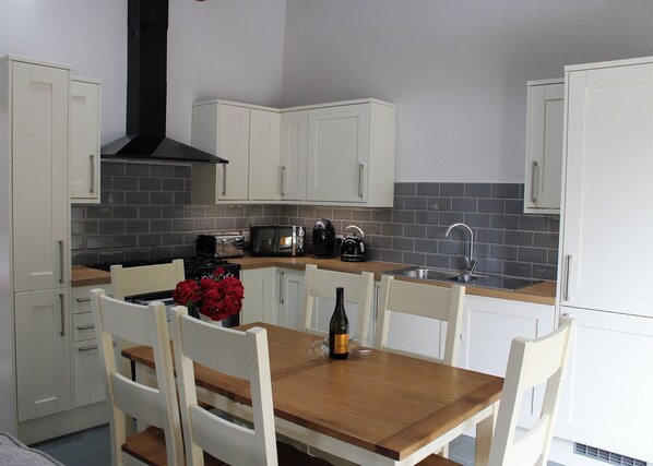 A kitchen with white cabinets, a wooden table, and a black range hood. - Our Grade II listed converted barn, The Croft. (Bassenthwaite, Keswick)