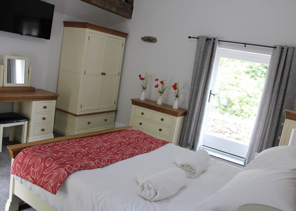 A bedroom with a bed, a dresser, a mirror, a television, and a window with curtains.