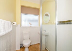 Ein Badezimmer mit Toilette, Waschbecken, Dusche und einem Fenster mit Vogel am Sims.