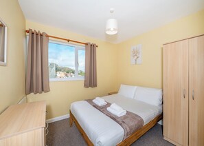 A bedroom with a bed, a wardrobe, a desk, a window with curtains, and a hanging light fixture.