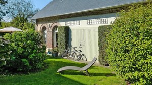 Een huis met een bakstenen boog, een fiets geparkeerd ervoor en een ligstoel op de voorgrond.